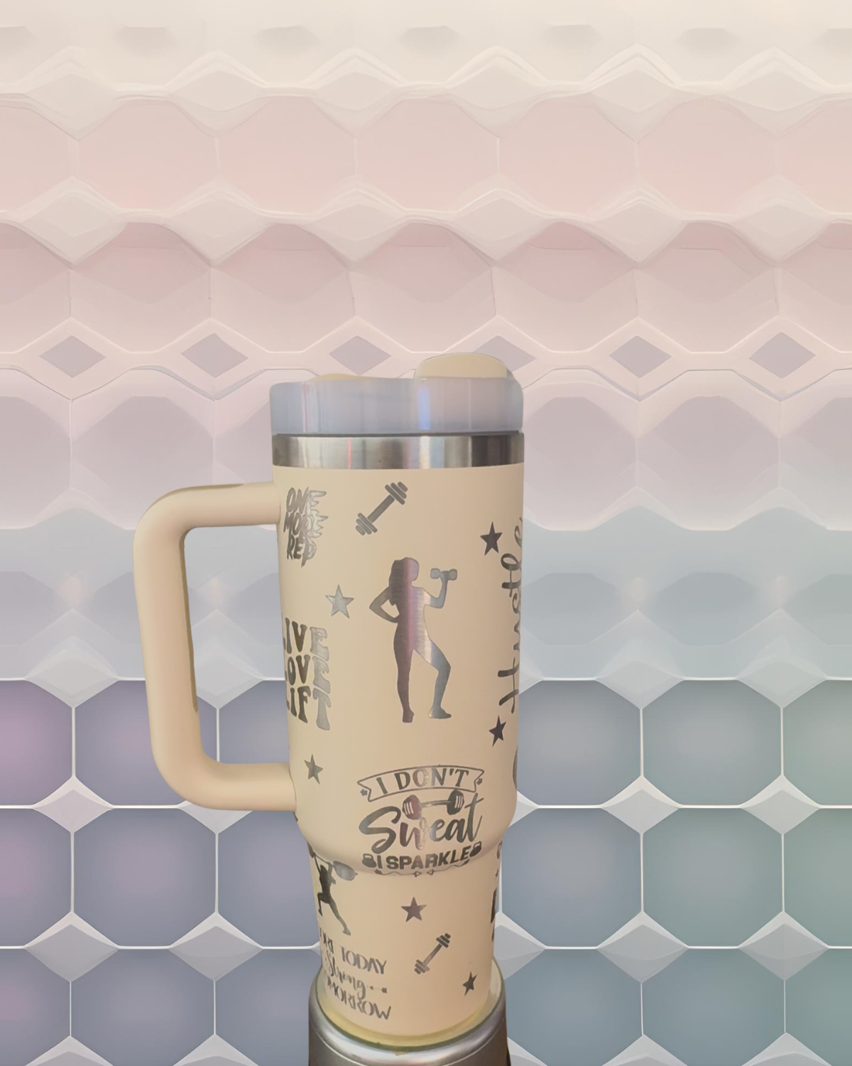 A beige insulated tumbler mug with various fitness-related designs and text printed on it, placed against a colorful geometric background.