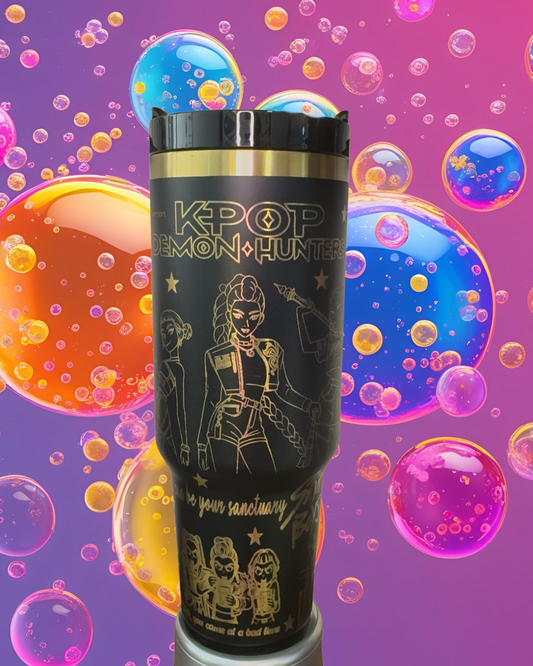 A black tumbler with a gold lid, featuring an illustration of a character from the Korean pop group K-popemon Hunter, surrounded by colorful bubbles.